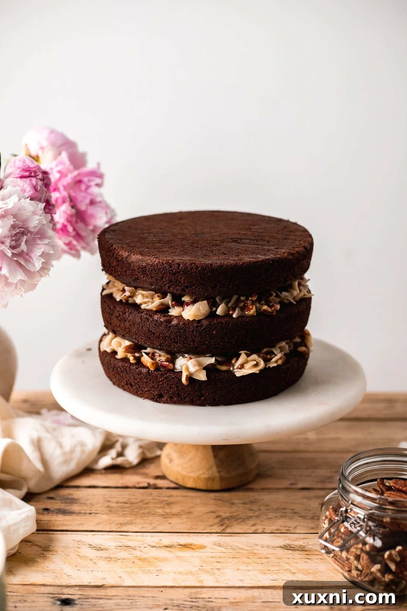 Assembling the vegan German chocolate cake with layers of chocolate cake and coconut pecan filling.