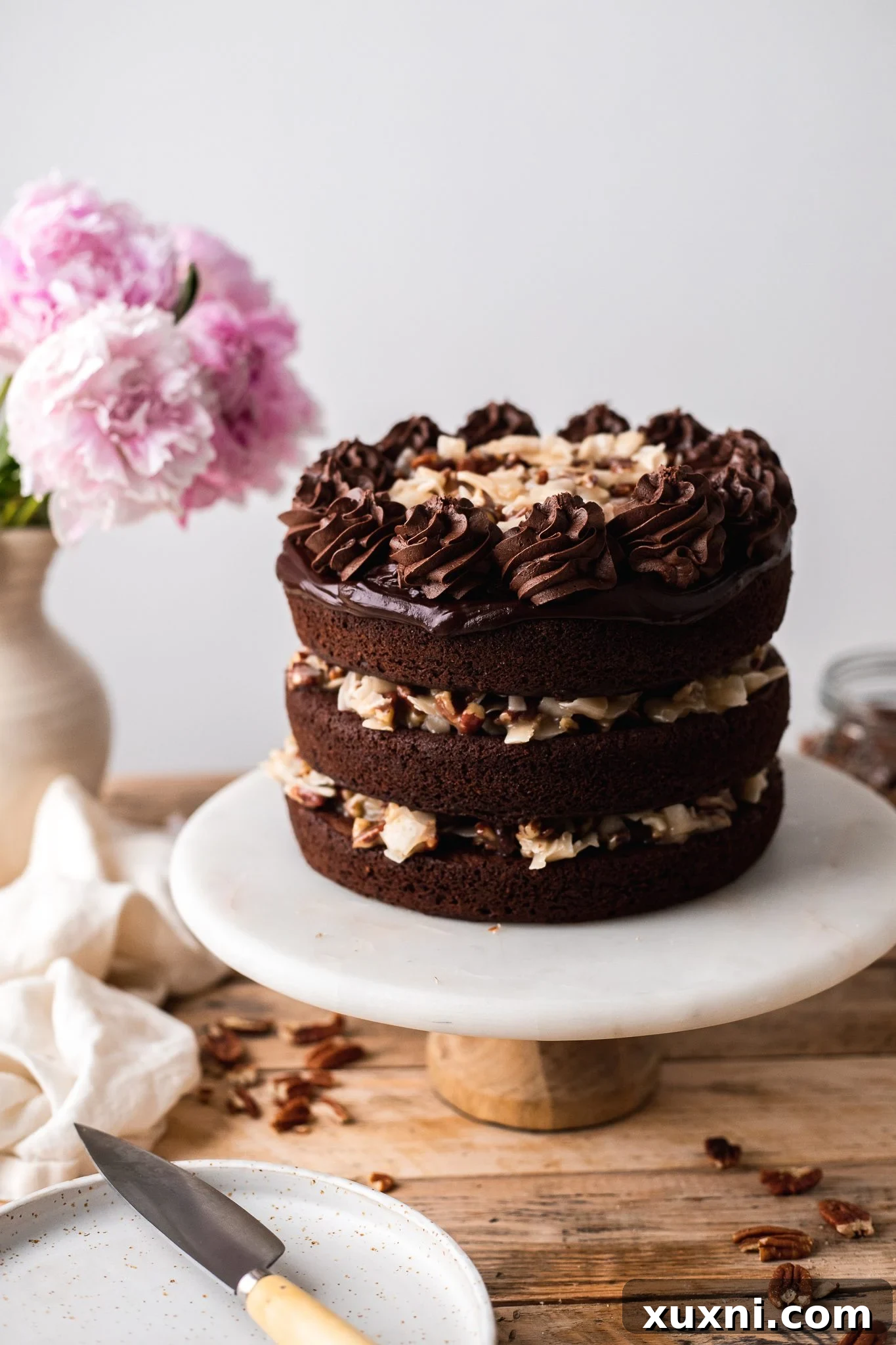 Decorated vegan German chocolate cake with piped chocolate buttercream and additional coconut pecan topping.