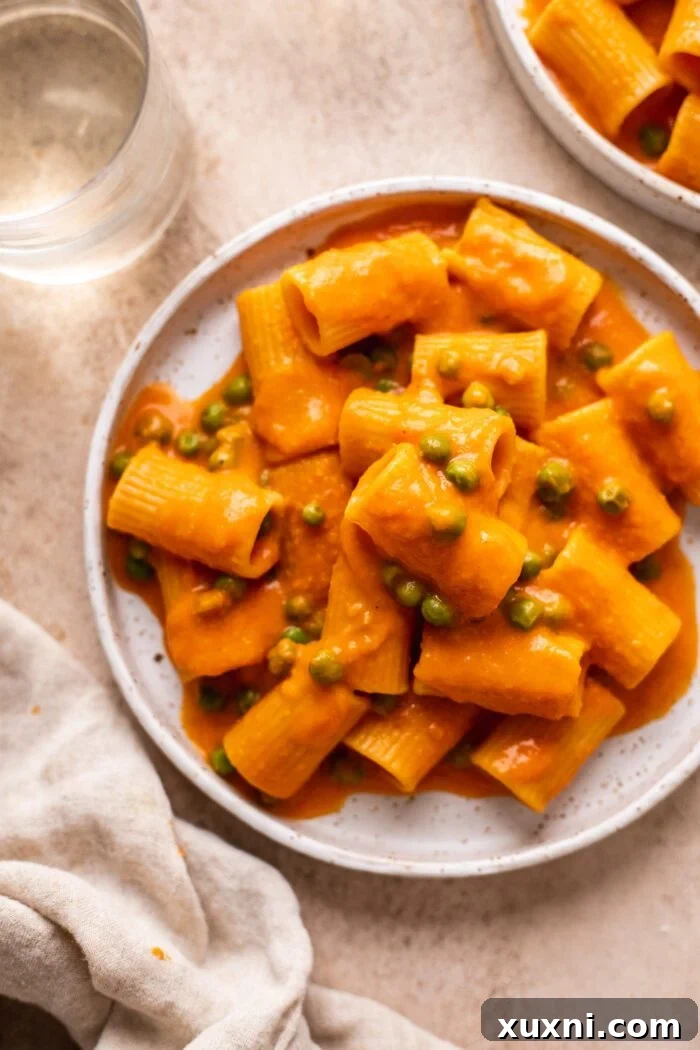 A vibrant bowl of vegan penne alla vodka, garnished with fresh peas and basil, ready to be enjoyed.