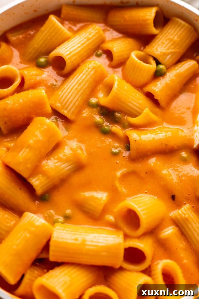 Close-up of the vegan vodka sauce and cooked pasta being tossed together in a large pan, creating a harmonious dish.