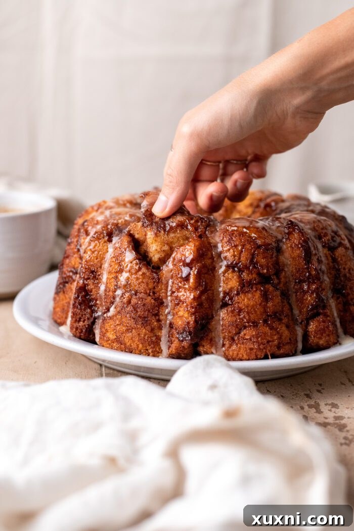 The Classic Soft and Fluffy Gluten-Free Monkey Bread 3 A hand gently pulling apart a piece of warm, sticky gluten-free monkey bread, showcasing its gooey cinnamon layers.