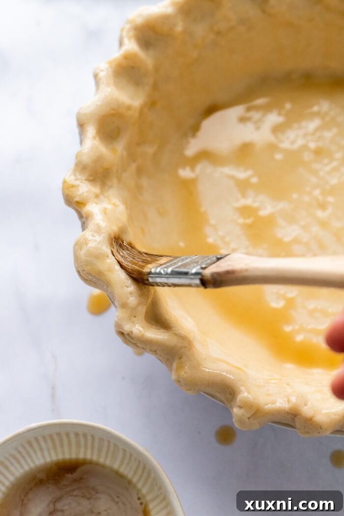 Brushing vegan egg wash onto the crimped edges of an unbaked gluten-free pie crust.