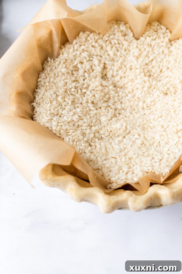 Unbaked gluten-free pie crust with parchment paper and pie weights, ready for baking.