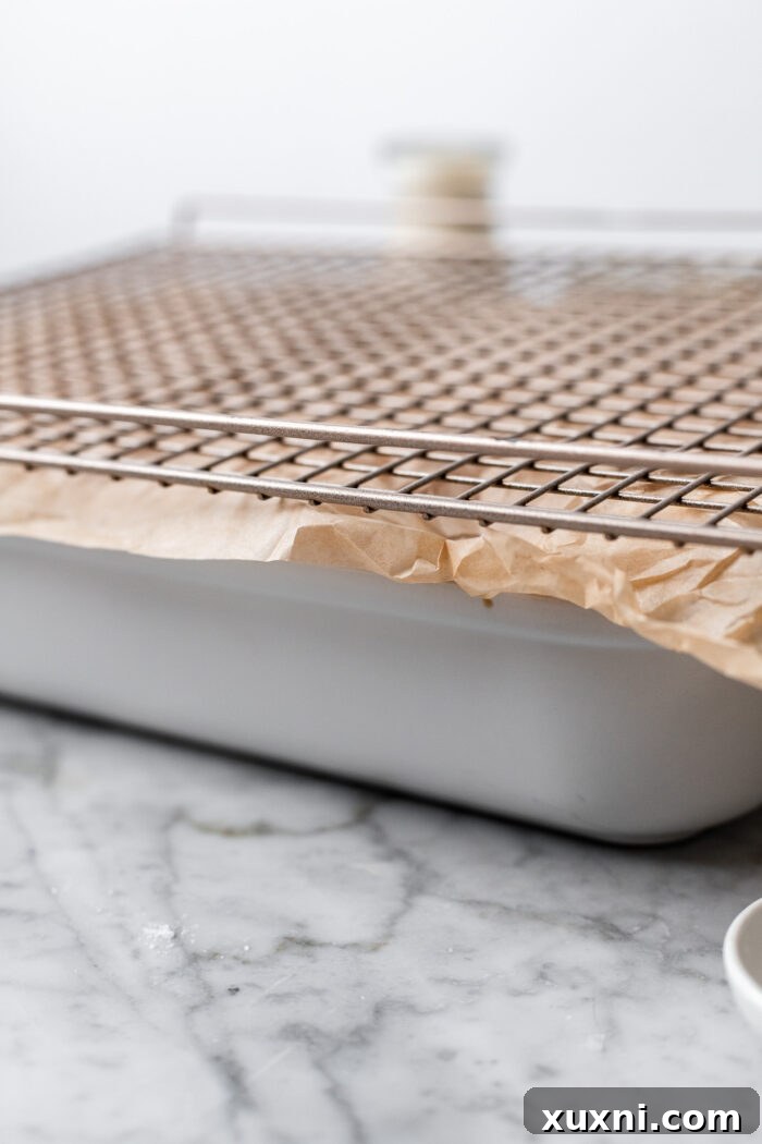 Set up for how to flip the sticky buns. The casserole dish is on bottom, followed by parchment paper, followed by a cooling rack on a marble table.
