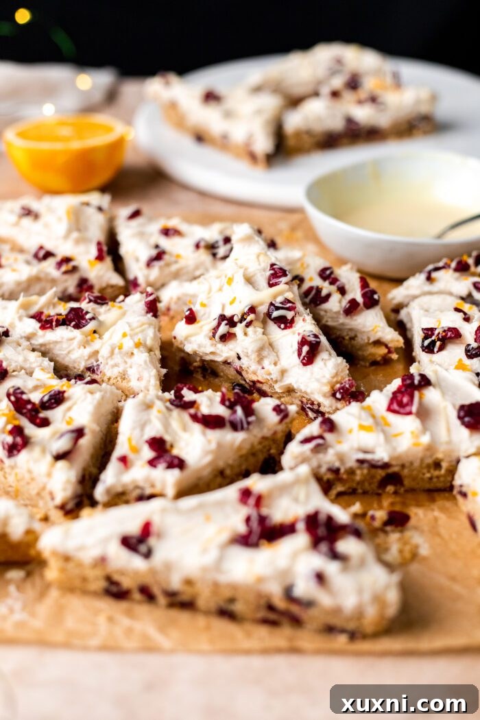 sliced cranberry bliss bars on a marble slab and parchment paper, showcasing the frosting and toppings