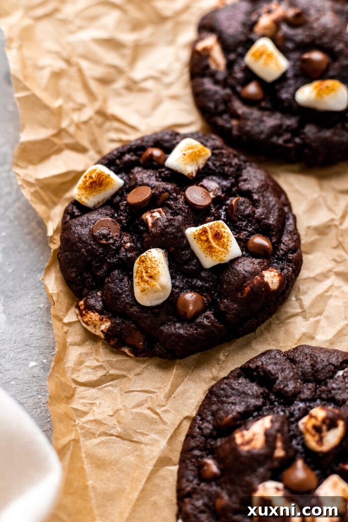 Hot cocoa cookies with melted marshmallows and chocolate on parchment paper, ready to be enjoyed.