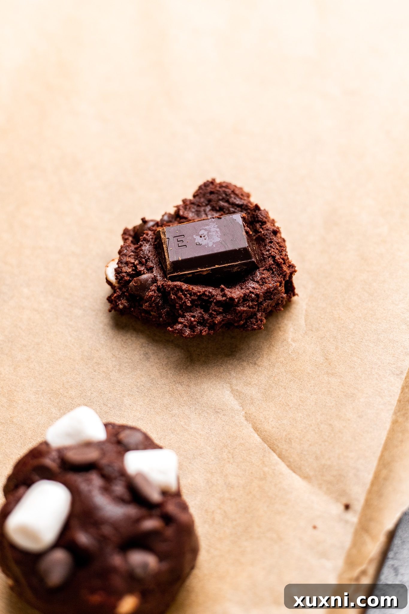 Hands pressing a chocolate square into cookie dough, preparing for the molten center.