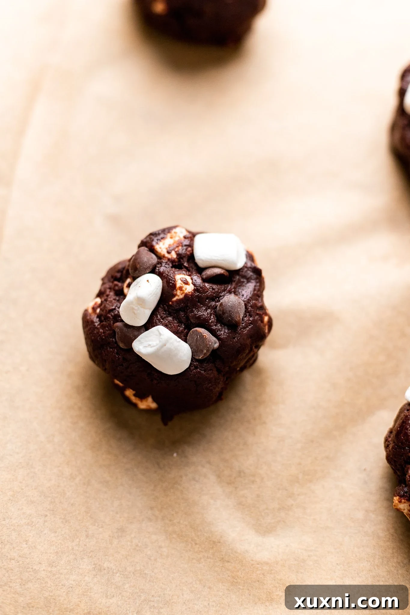 Hot cocoa cookie dough balls with marshmallows pressed on top, ready for baking.