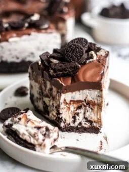 A close-up of a partially eaten slice of vegan Oreo cheesecake, showing the layers of crust, creamy filling with cookie chunks, and a drizzle of chocolate ganache.