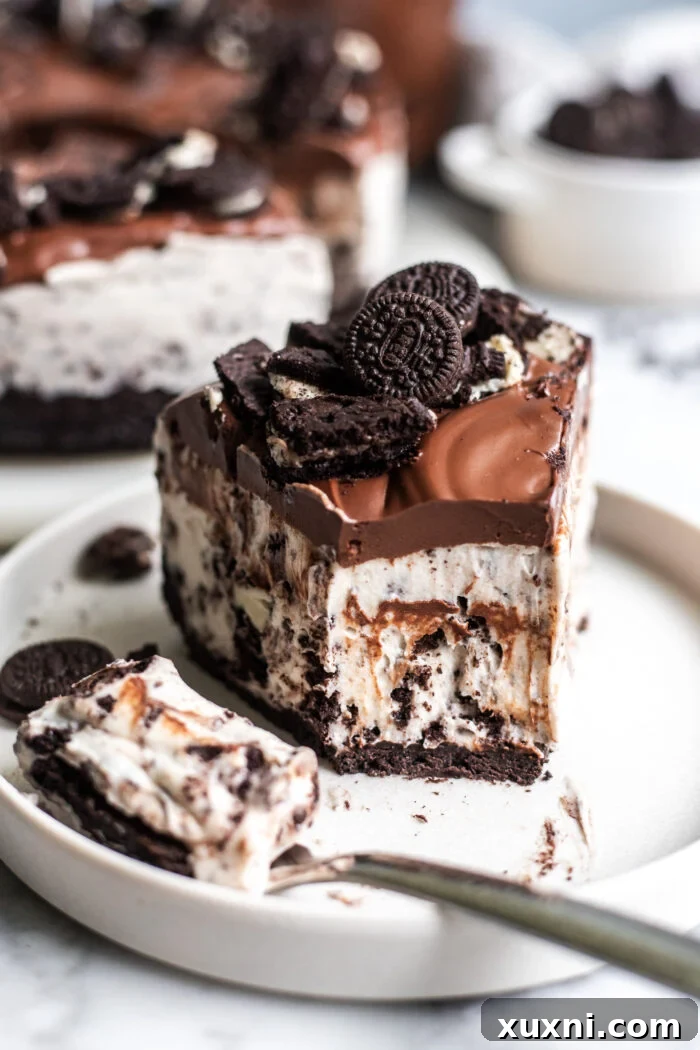 A close-up of a partially eaten slice of vegan Oreo cheesecake, showing the layers of crust, creamy filling with cookie chunks, and a drizzle of chocolate ganache.