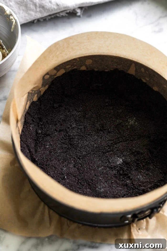 The crushed Oreo cookie crust pressed firmly into the bottom of a springform pan, showing a smooth and even base.