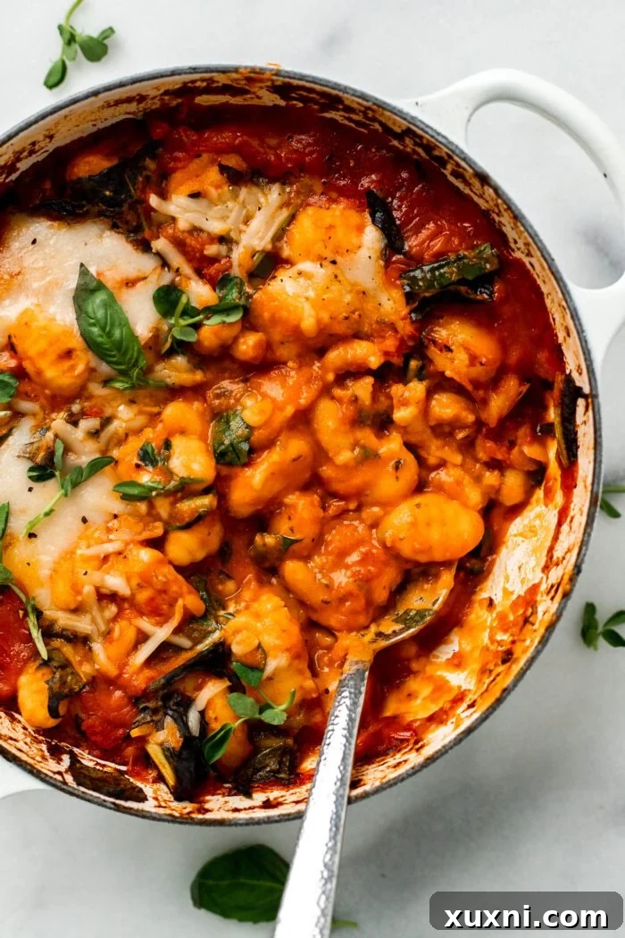 25-Minute No-Boil Vegan Cheesy Baked Gnocchi with Beans 3 A serving spoon lifting a spoonful of gooey, cheesy baked gnocchi from the dish.