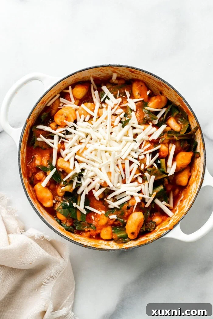 25-Minute No-Boil Vegan Cheesy Baked Gnocchi with Beans 10 Shredded vegan cheese being stirred into the baked gnocchi mixture.