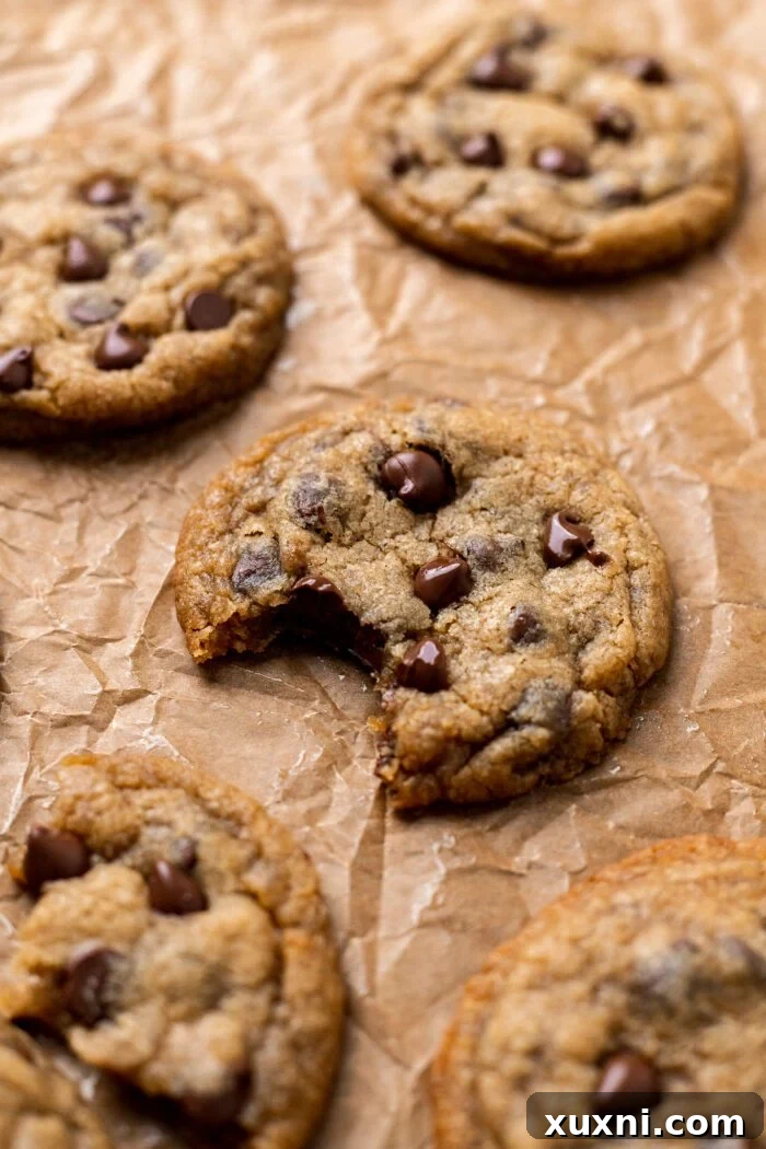 A vegan chocolate chip cookie with a bite taken out, showing its soft interior and melted chocolate, on parchment paper.