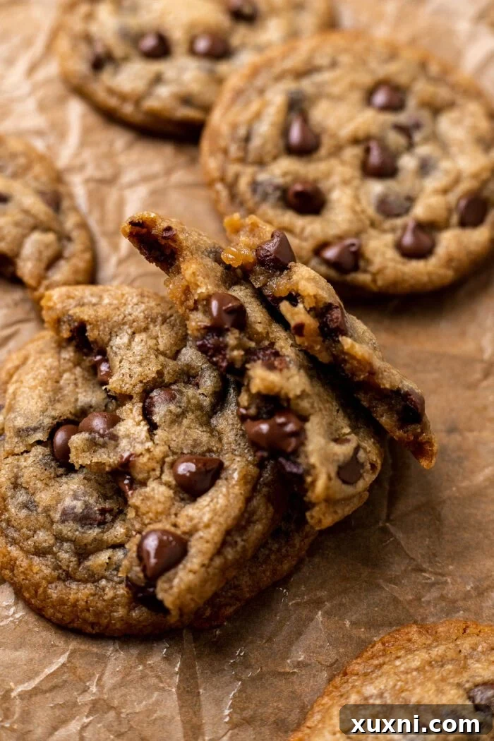 Stack of two halved chocolate chip cookies revealing their soft, melty chocolate centers on parchment paper.