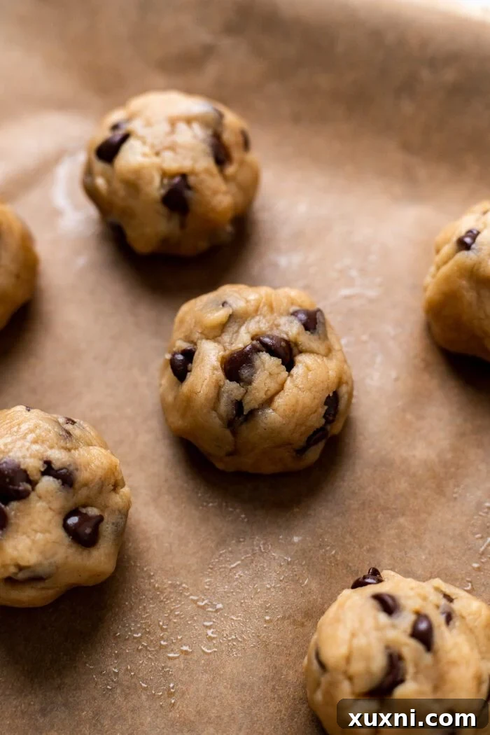 Scooped chocolate chip cookie dough balls arranged on a parchment-lined baking sheet, spaced for even baking.
