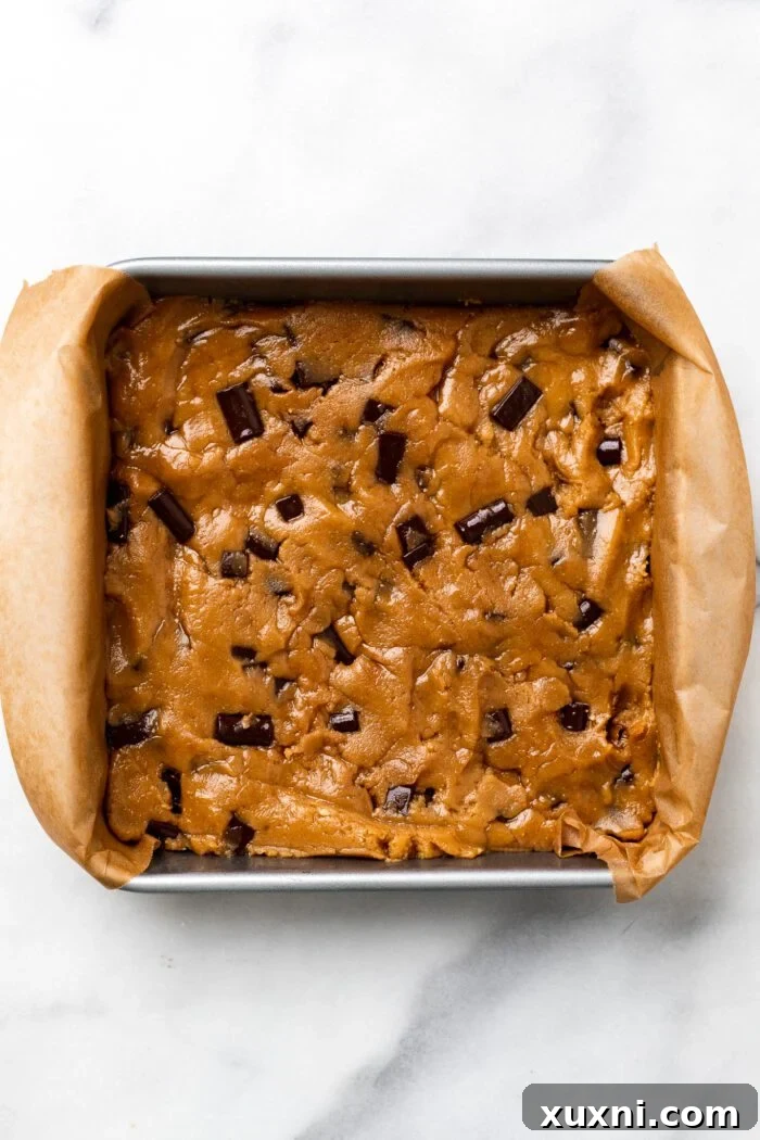 Peanut butter blondie dough pressed into a parchment-lined baking pan before baking