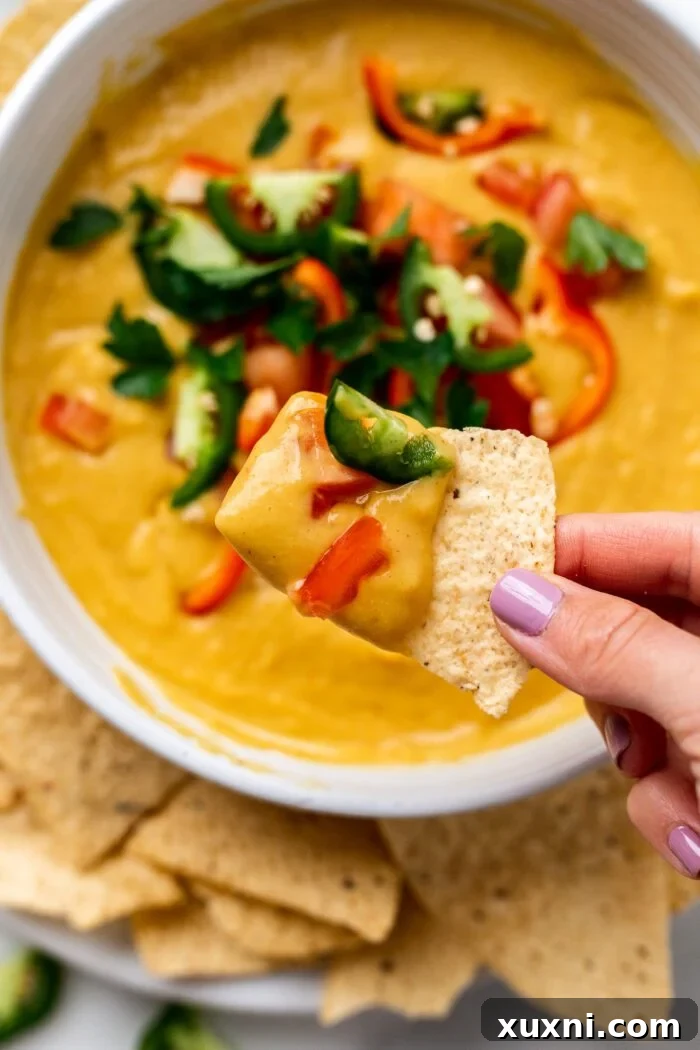 tortilla chip dipping into a fully garnished bowl of vegan queso