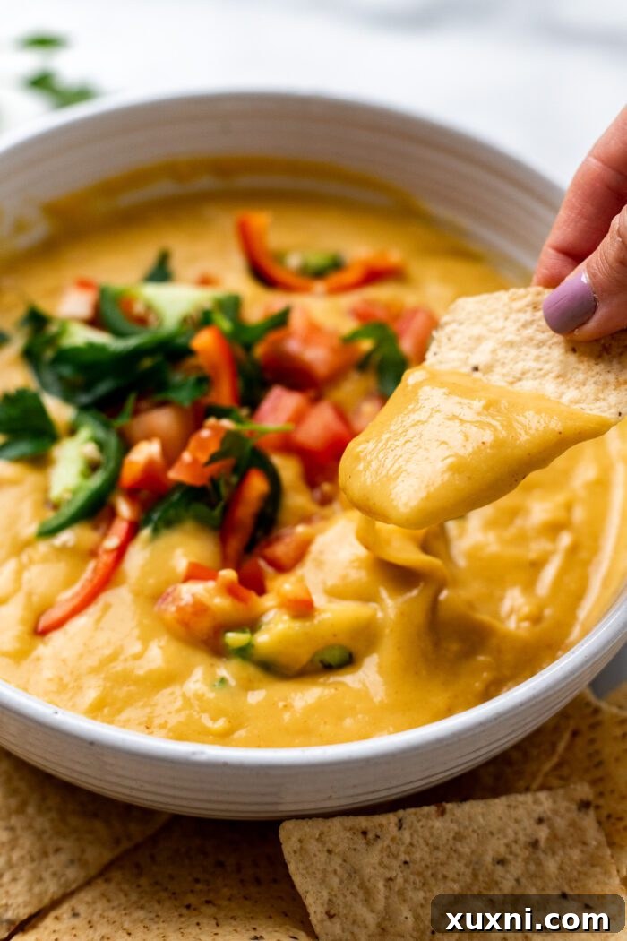 tortilla chip dipping into a bowl of creamy vegan Queso