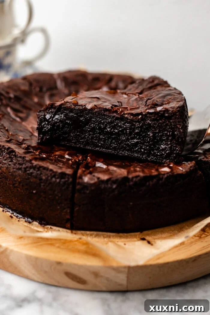 Multiple slices of vegan flourless chocolate cake stacked on a white background, highlighting their moist texture.