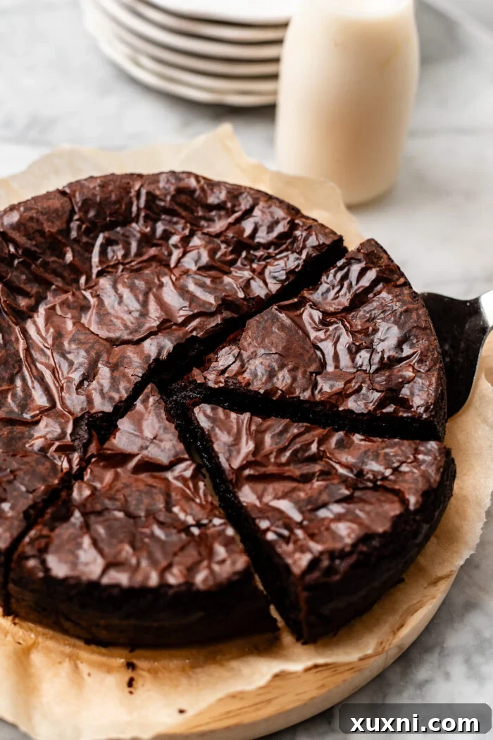A slice of vegan flourless chocolate cake with a spoon, showing its dense, moist texture and glossy appearance.