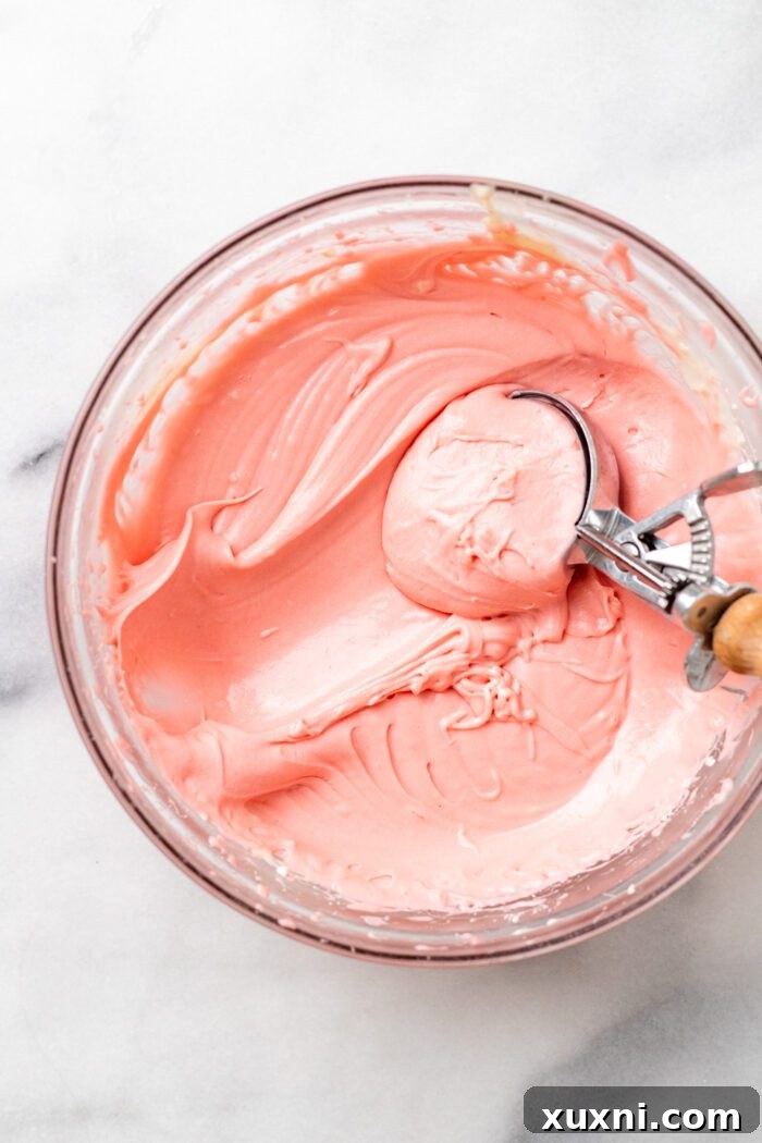 Vegan cream cheese frosting, dyed a vibrant pink, in a bowl with a spatula, ready to be spread.