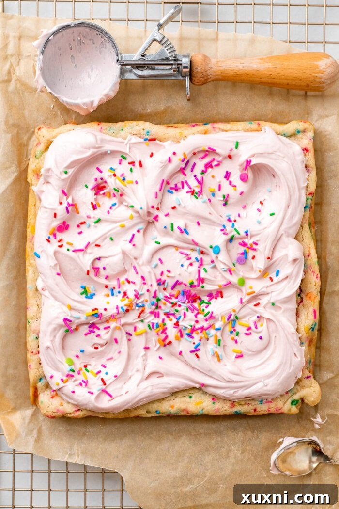 Fully frosted vegan sugar cookie bars topped with colorful sprinkles, ready to be cut and served.