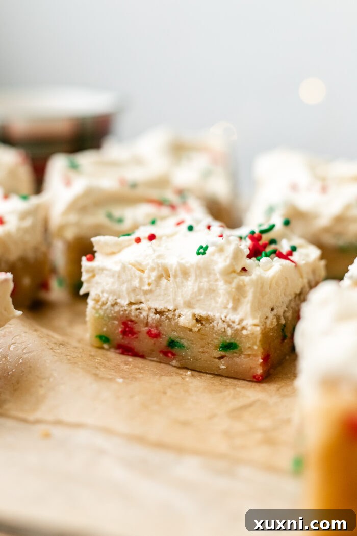 A festive holiday-themed vegan sugar cookie bar, frosted and topped with colorful sprinkles, held ready to be enjoyed.