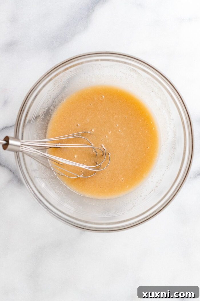 Wet ingredients (vegan butter, sugar, yogurt, vanilla, almond extract) being whisked together in a bowl until smooth and creamy.