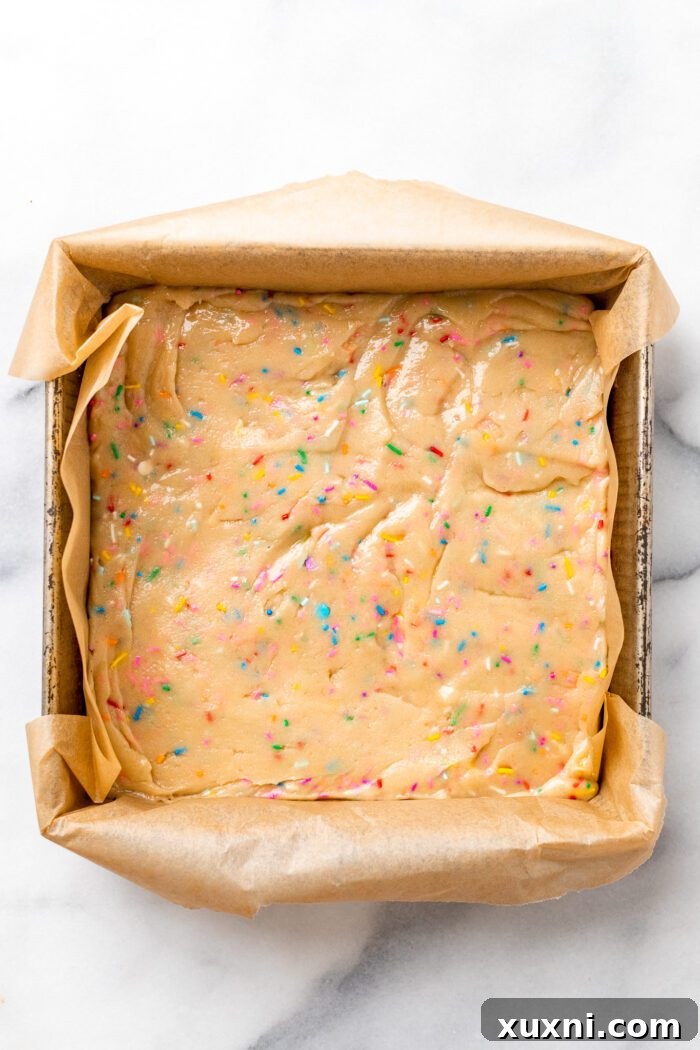 Unbaked cookie dough pressed evenly into an 8x8 baking pan lined with parchment paper.