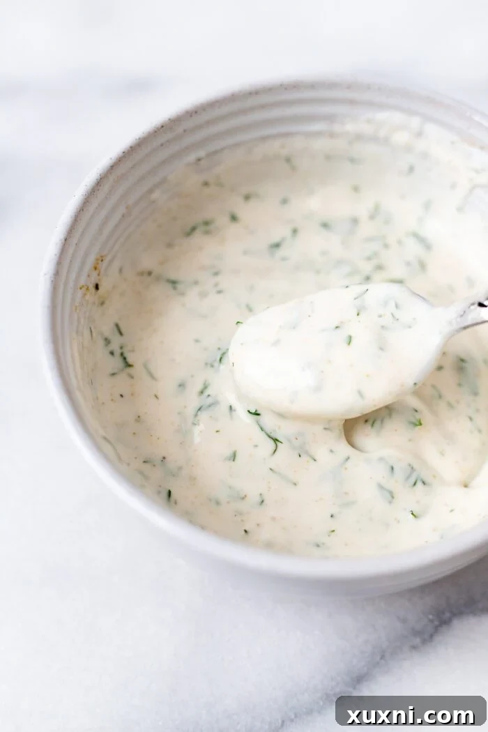 bowl of yogurt dill sauce with a spoon in it, garnished with fresh dill