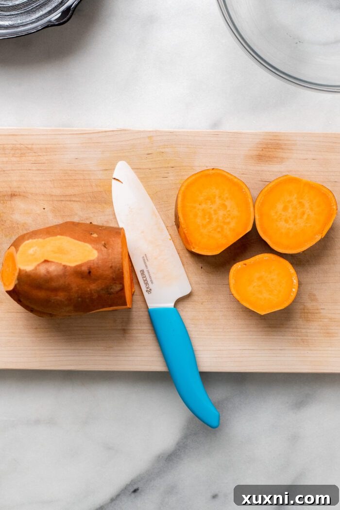 Sweet potatoes sliced in half lengthwise on a cutting board, ready for dicing into rounds.