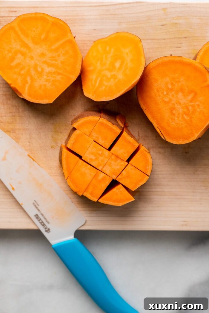 Sweet potato rounds being precisely cut into uniform cubes on a cutting board, ready for seasoning.