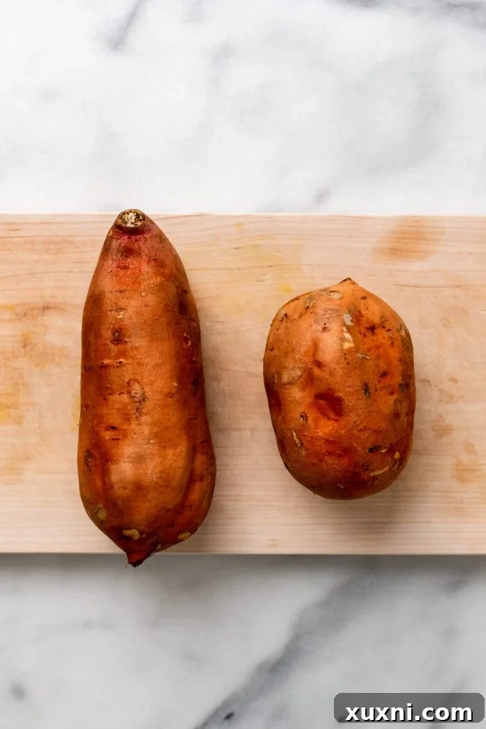 Freshly washed sweet potatoes on a white cutting board, showing their clean, vibrant skins.