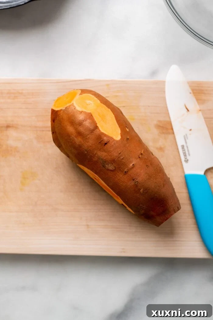 A sweet potato on a cutting board, with small blemishes being removed before the cubing process.