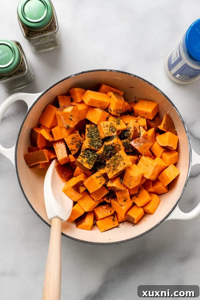 Sweet potato cubes generously seasoned with herbs, salt, pepper, and melted vegan butter in a Dutch oven.
