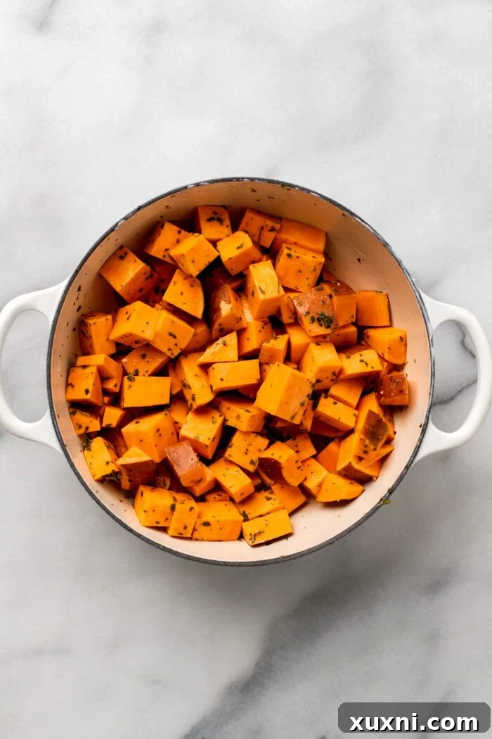 Sweet potato cubes being gently tossed with seasonings in a Dutch oven to ensure every piece is evenly coated.