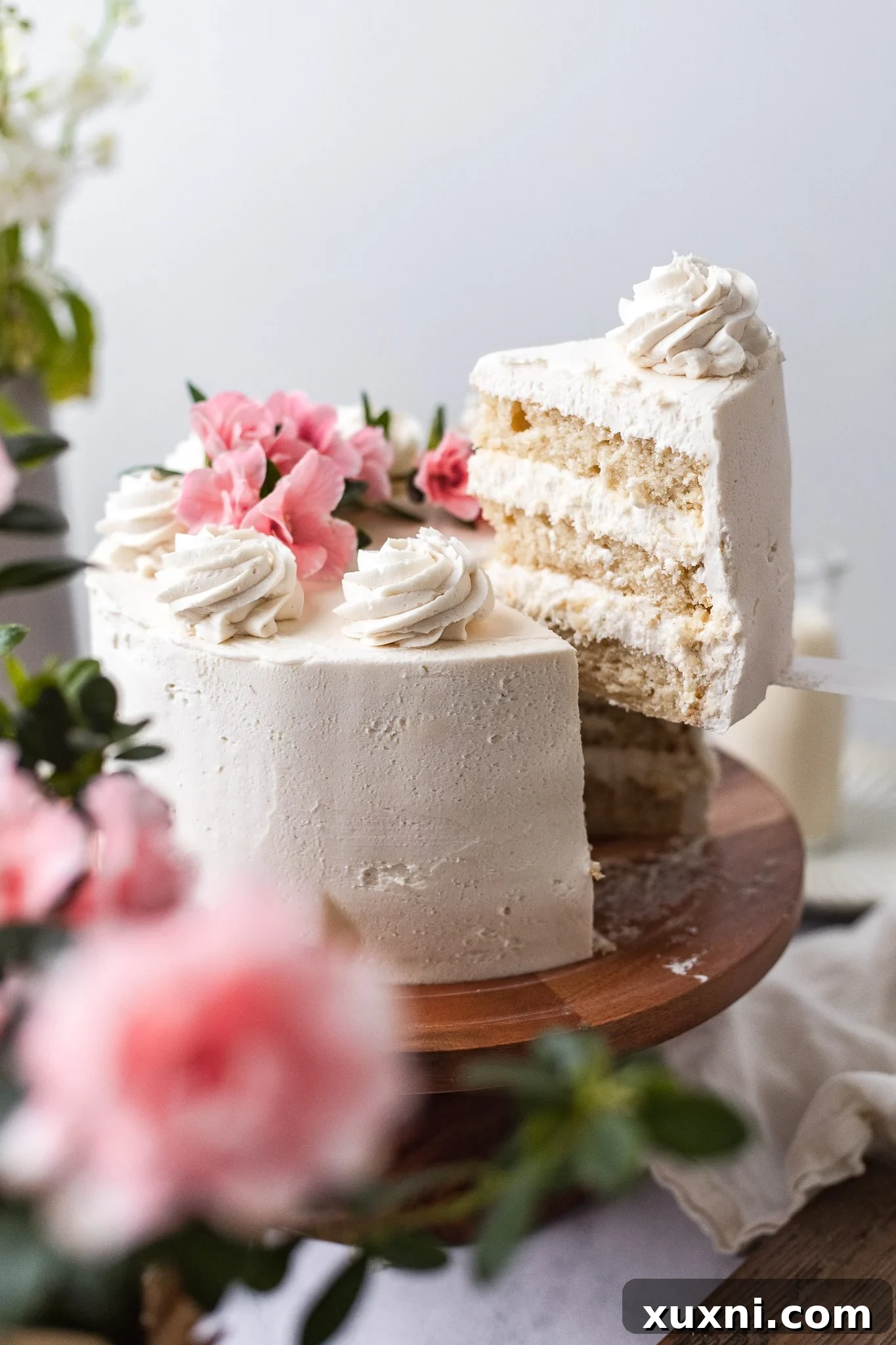 A slice of vegan vanilla cake being gently lifted from the whole cake, revealing layered frosting.