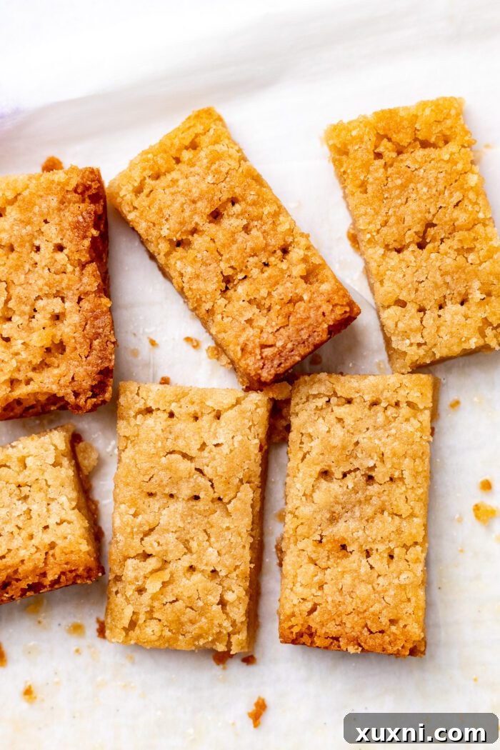 A close-up of perfectly sliced shortbread biscuits with fork marks on a cutting board.