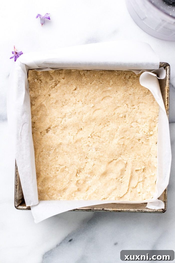 Shortbread dough pressed firmly and evenly into a parchment-lined square baking pan.