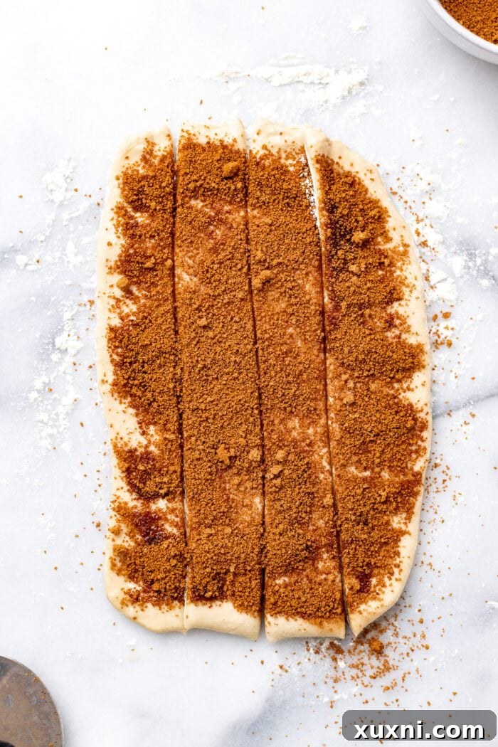 Vegan cinnamon roll dough sliced into four even strips, ready to be rolled individually