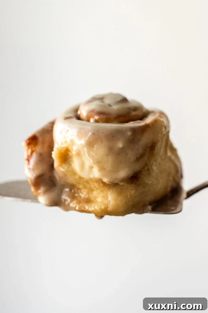 A vegan cinnamon roll being served with a pie server, showing its gooey texture and generous frosting