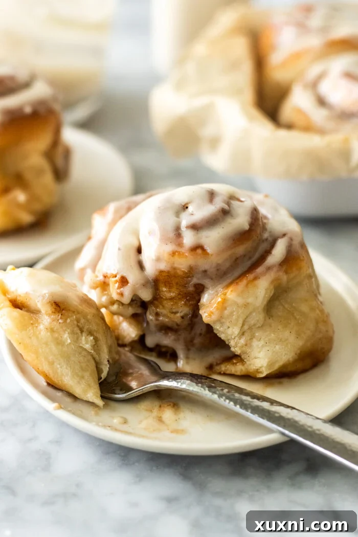 Close-up of a bitten browned vegan butter cinnamon roll on a white plate, revealing the rich filling and fluffy interior