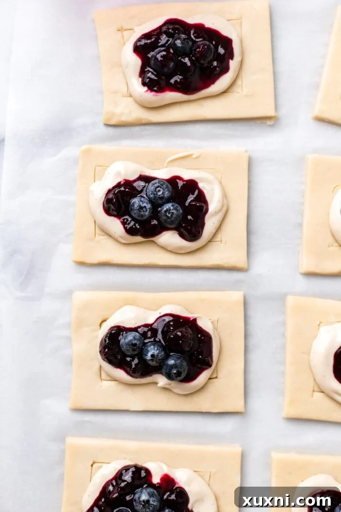 Topping the cream cheese filling with blueberry jam and fresh blueberries.