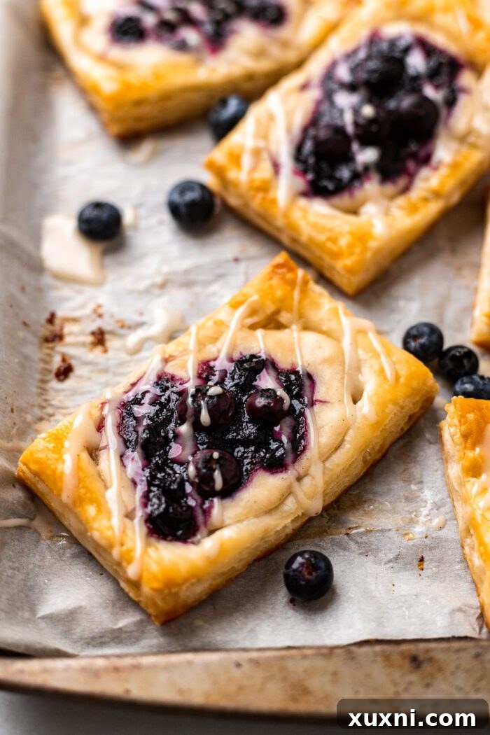Freshly baked blueberry Danish pastries cooling on parchment paper, ready for glazing.