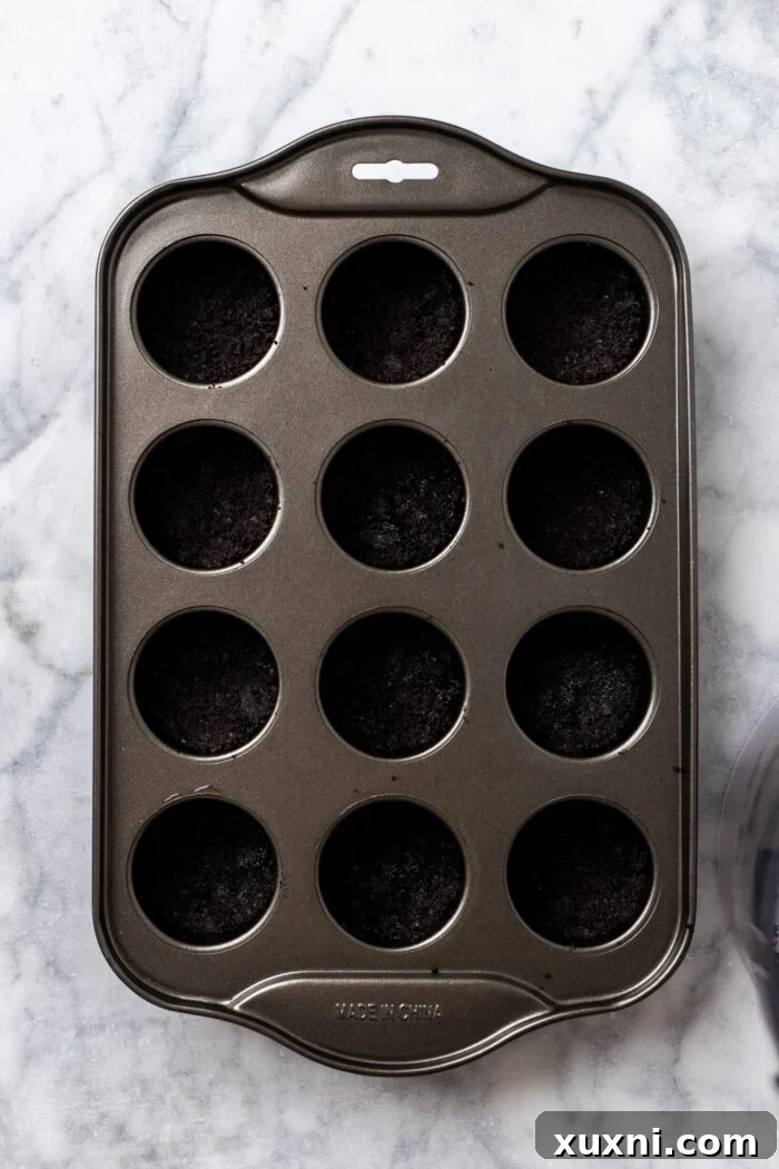 Easy No Bake Plant Based Chocolate Mini Cheesecakes 6 Chocolate cookie crumbles being pressed firmly into the bottom of mini cheesecake pans, forming the base layer.