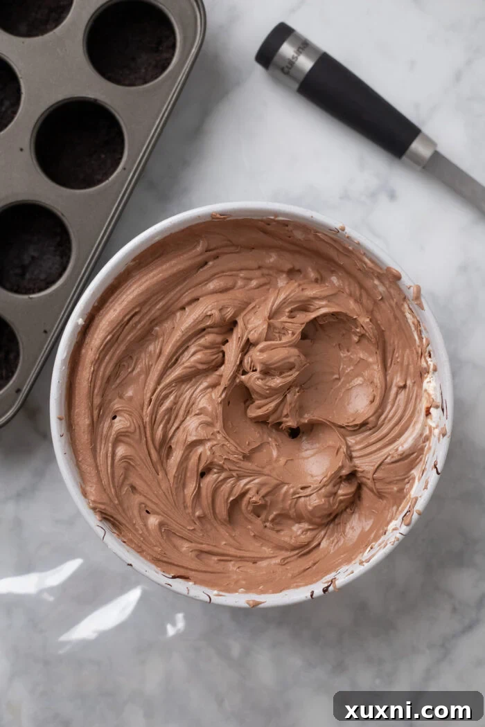 Easy No Bake Plant Based Chocolate Mini Cheesecakes 9 Assembled ingredients for mini chocolate cheesecakes, including the crusts in pans and the chocolate filling in a piping bag, laid out on a marble surface.