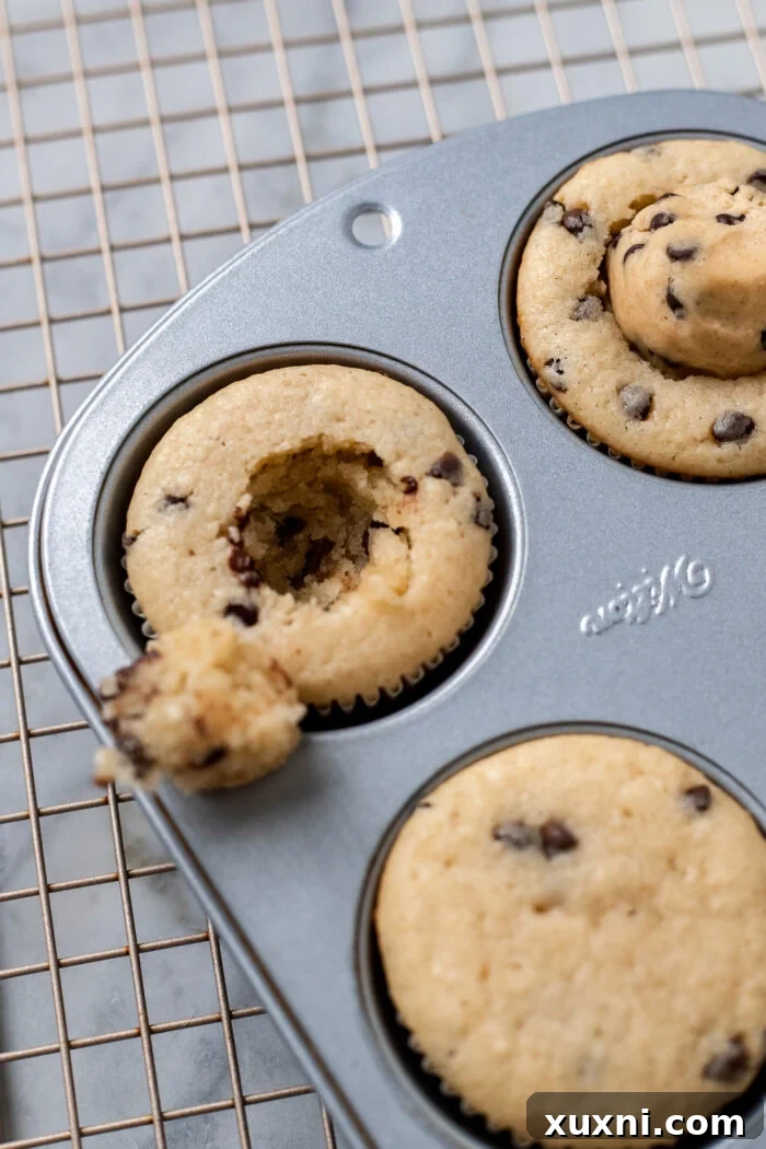 Cored chocolate chip cupcakes in a muffin tin, creating a cavity for the cookie dough filling.