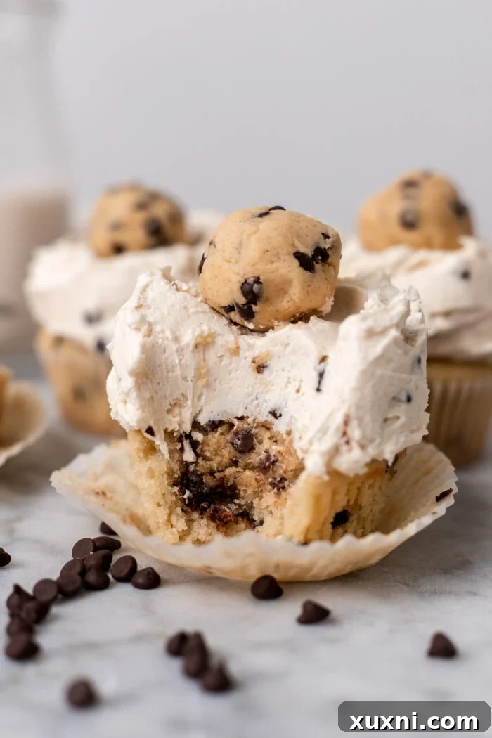 Close-up of a perfectly baked and frosted cookie dough cupcake, partially bitten, on a marble surface.