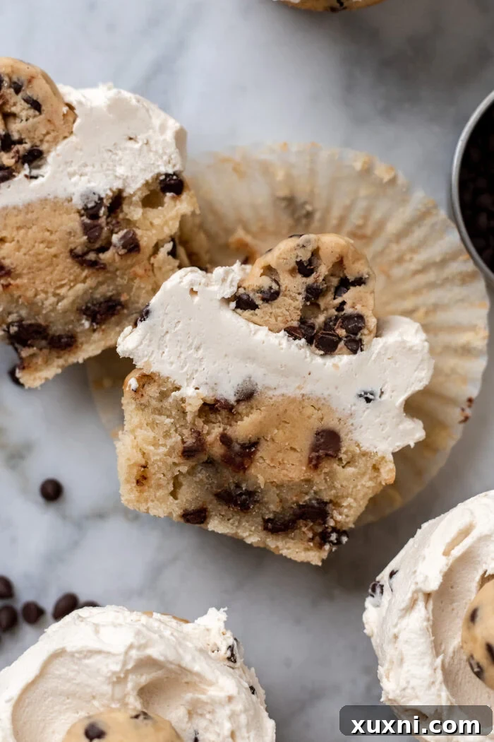 A cookie dough cupcake sliced in half, showcasing the distinct layers of cupcake, molten cookie dough filling, and frosting.